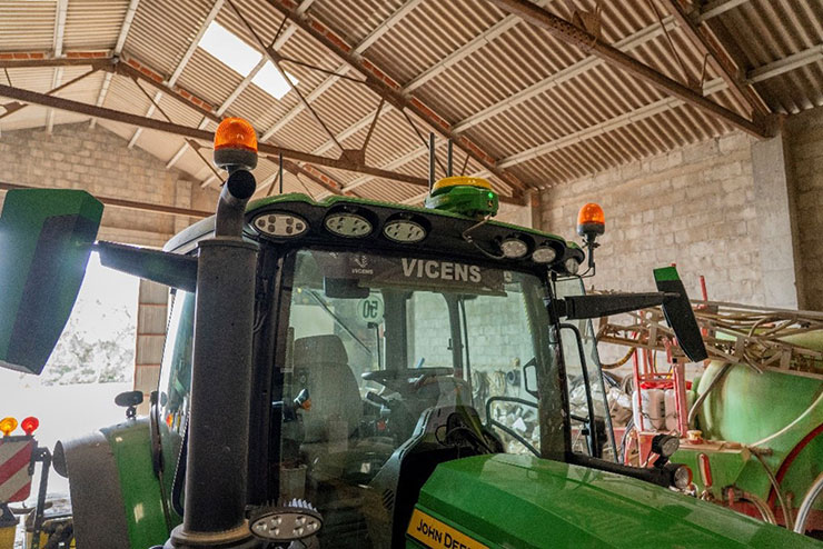 Tractor agrícola amb equip de posicionament GNSS al sostre de la cabina, dins d'una nau.