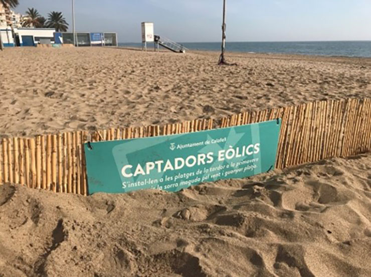 Tanca de fusta amb un cartell de l'Ajuntament de Calafell sobre "captadors eòlics", instal·lada a la sorra d'una platja per afavorir la formació de dunes.