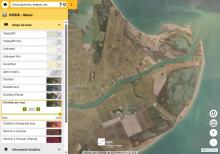 Orthophoto of the Ebro Delta showing geometric farmland, canals and coastal lagoons in green and brown tones, with the river's mouth in the Mediterranean Sea and several bluish bodies of water